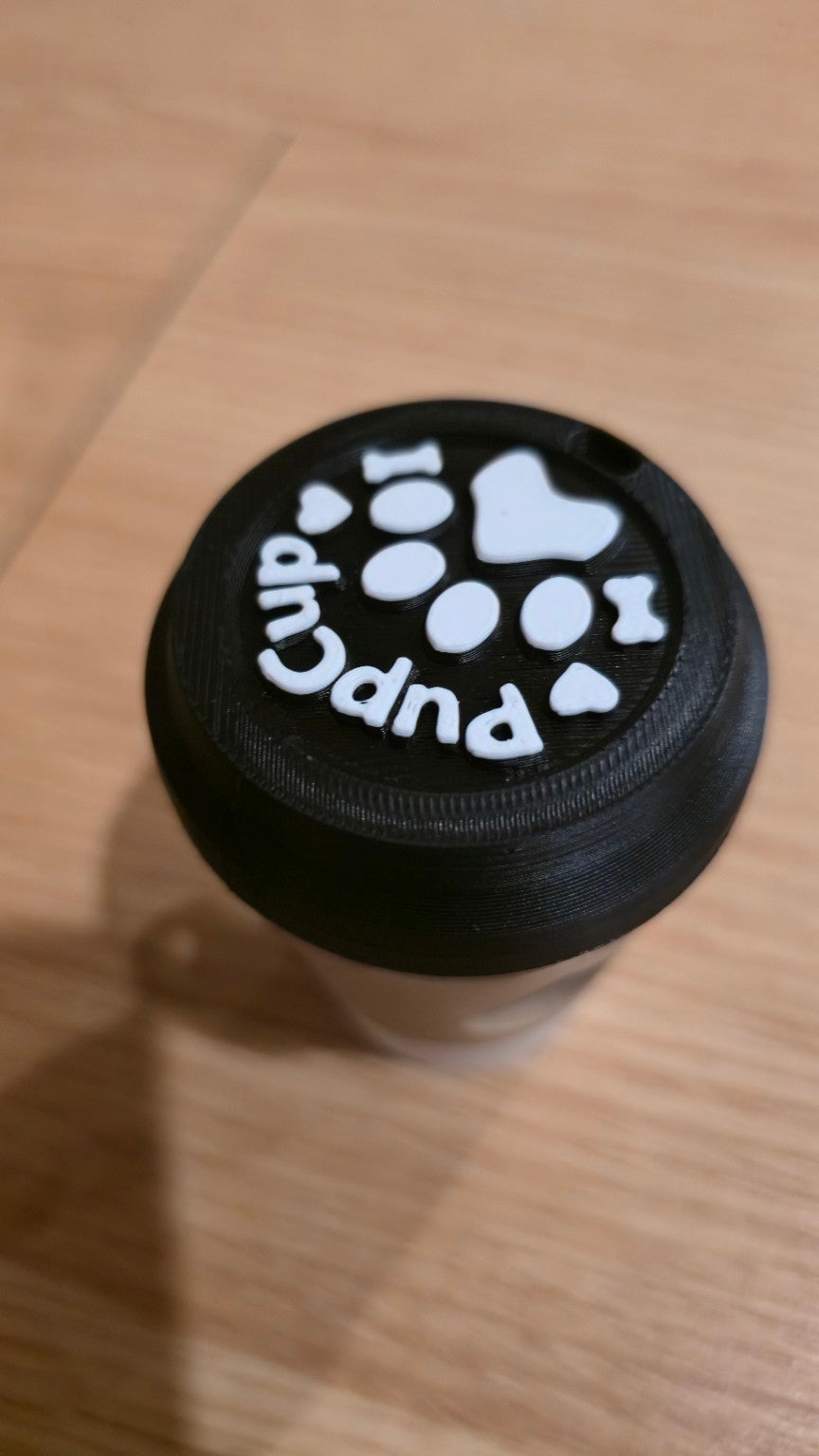 Close-up of black lid with raised white paw print and PupCup text